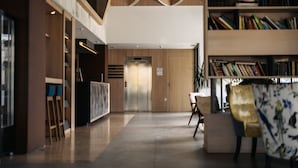 Un lobby moderno con un ascensor central, una mesa de recepción y una estantería llena de libros.