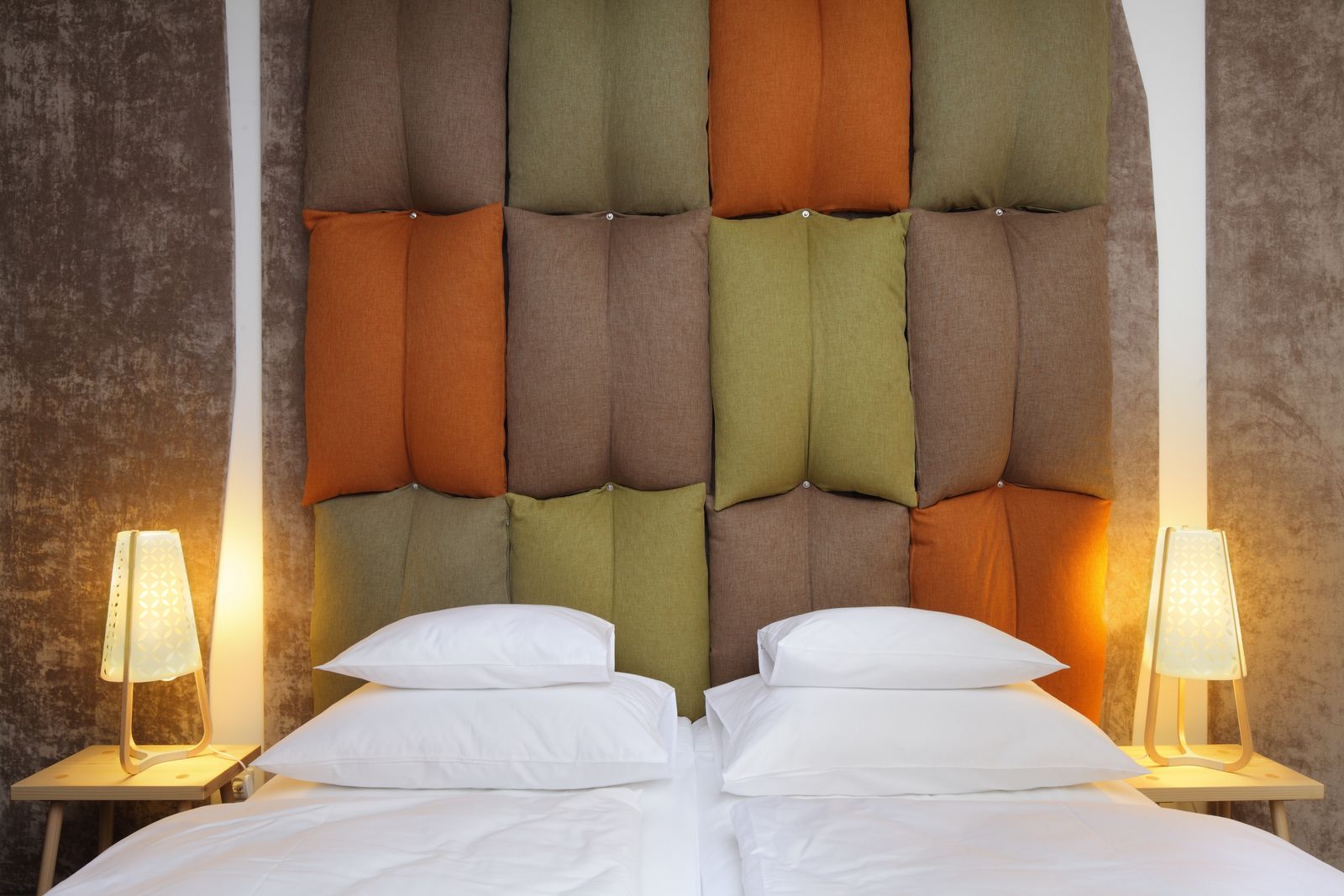Una cama con cabecera capitonada en varios colores, dos lámparas de noche y ropa de cama blanca.