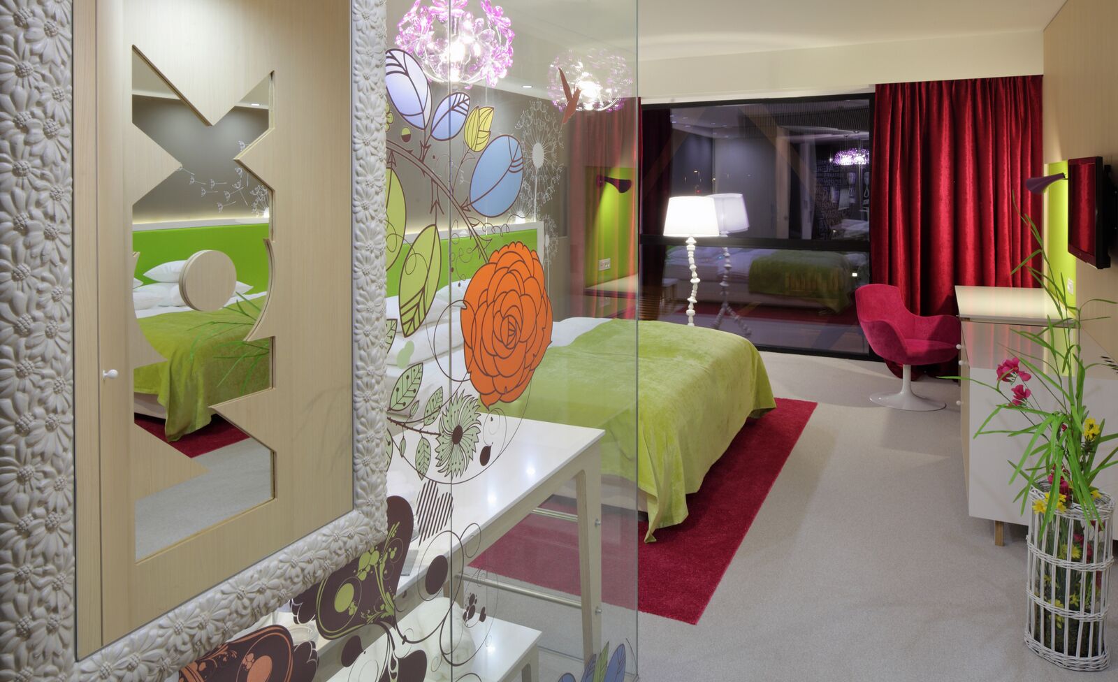 A hotel room with a bed, a desk, a chair, a mirror, and a red curtain.