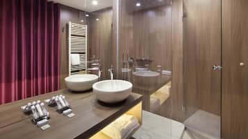 A modern bathroom with two large sinks, a glass shower enclosure, and a vanity with toiletries.