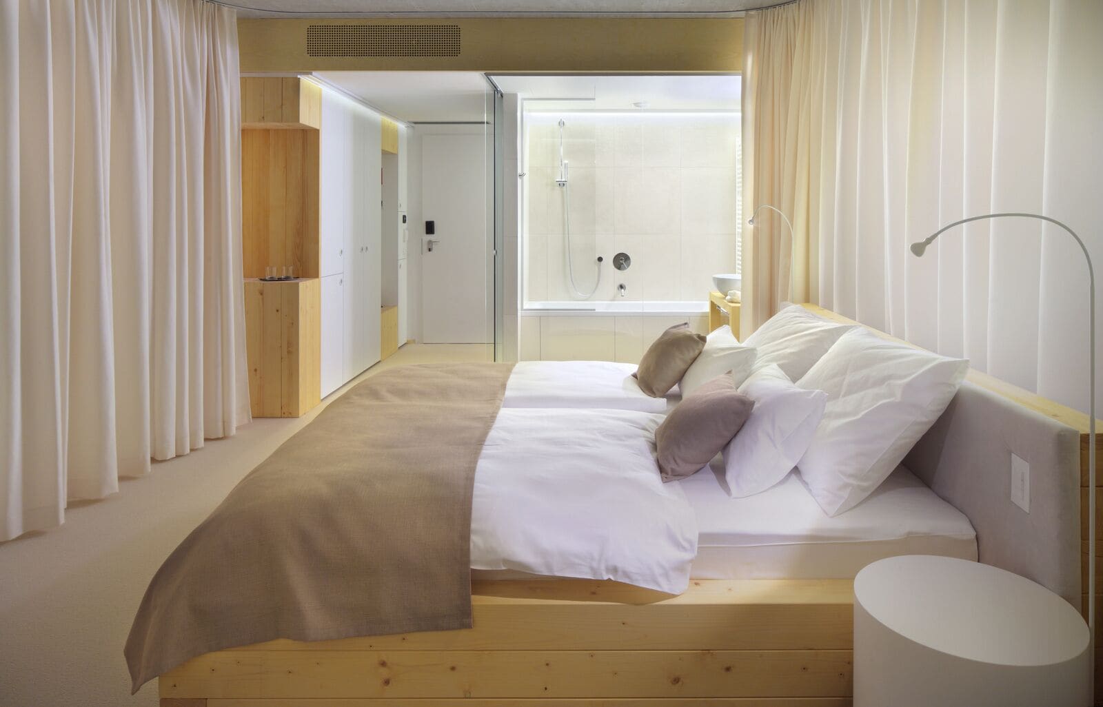 Une chambre à coucher comprenant un lit, une table de chevet, une lampe et donnant sur une salle de bain avec douche.