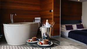 Un baño moderno con una bañera grande, una mesita con dos postres de chocolate y un cubo para champán.