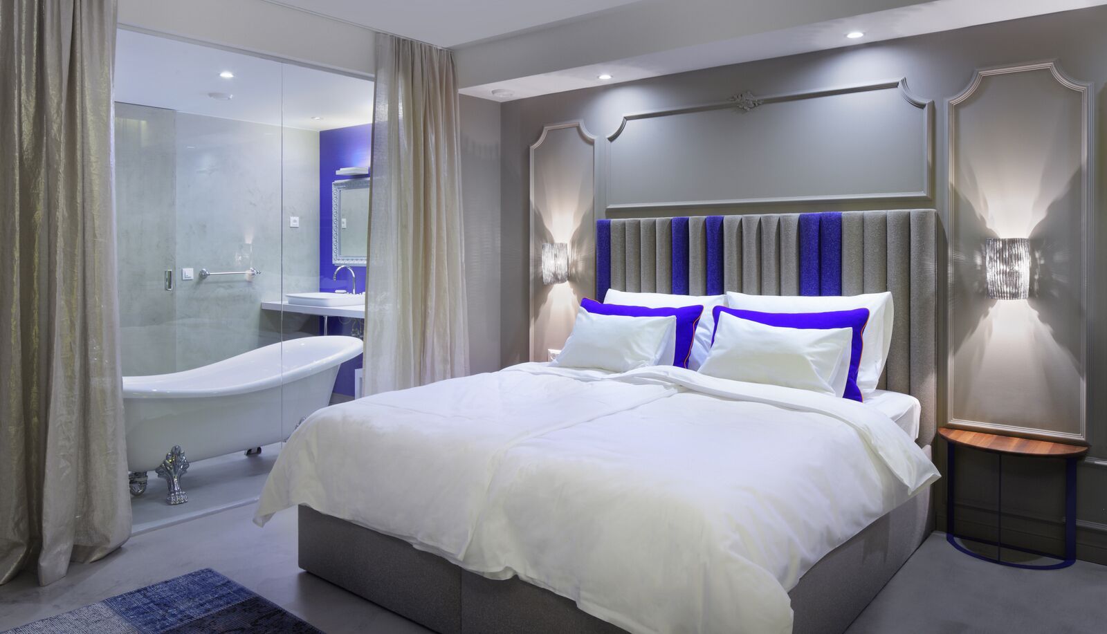 Ein modernes Hotelzimmer mit einem großen Bett, einem separaten Badezimmer mit einer Badewanne und einem kleinen Nachttisch.