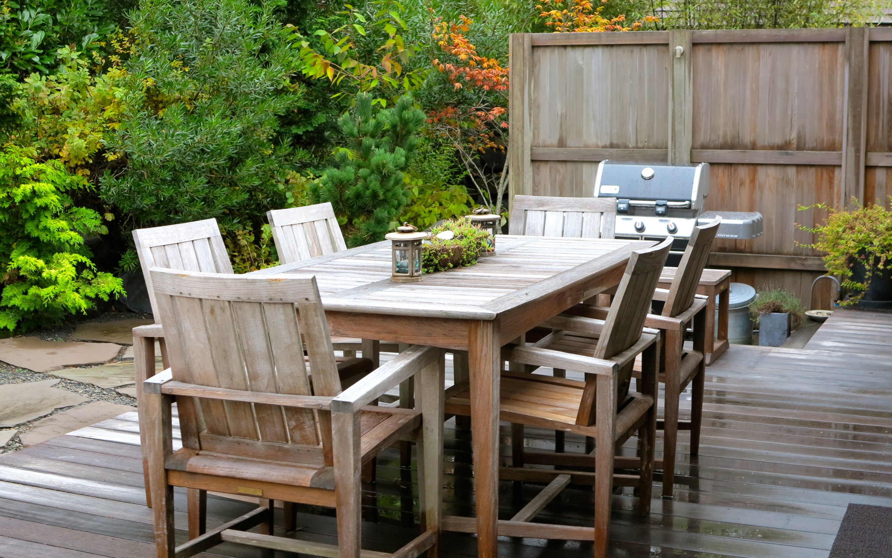 A wooden deck with a table and chairs, a grill, and a variety of plants.