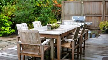 A wooden deck with a table and chairs, a grill, and a variety of plants.