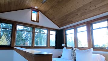 Una habitación con techo de madera, ventanas amplias, cama con ropa blanca y una almohada con forma de búho.