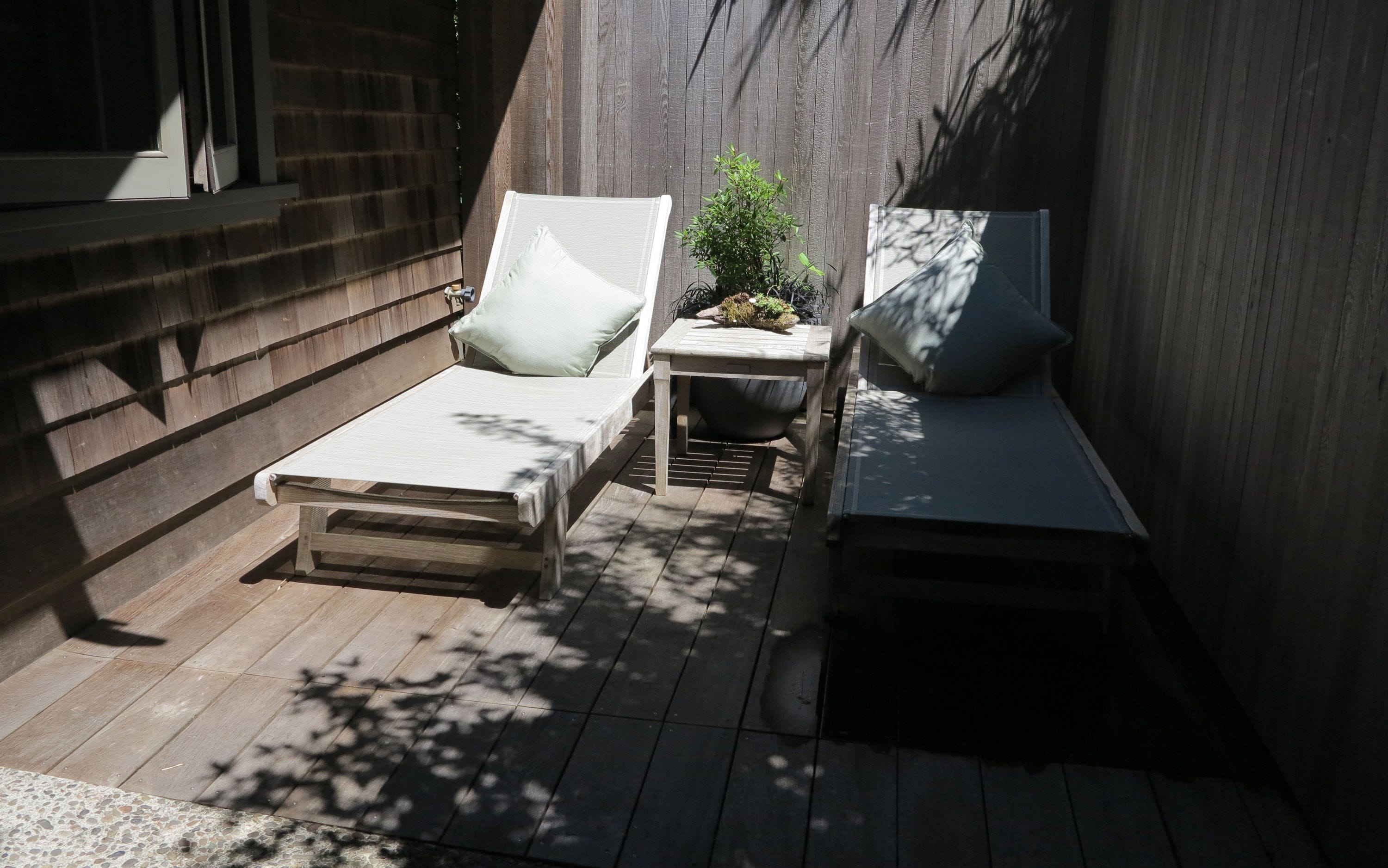 Uma pequena área externa com um deck de madeira, um banco estofado e uma mesa com uma planta.