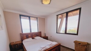 Ein Schlafzimmer mit einem hölzernen Bett, zwei Nachttischen, einem Beistelltisch, einem Korbwannen und zwei Fenstern mit Jalousien.
