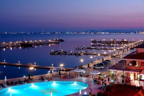 A marina with boats, a swimming pool, and a building with outdoor seating. - Family Hotel Venera (Nessebar)