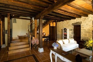 Un interior rústico con vigas de madera a la vista, una pared de piedra, un sofá blanco y una escalera que lleva a otra habitación.