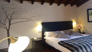 Hotelkamer met een bed, nachtkastje met lamp, telefoon aan de muur en een decoratieve muurschildering van een boom.