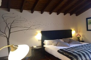 Habitación de hotel con cama, mesita de noche con lámpara, teléfono en la pared y un mural decorativo con motivos vegetales.