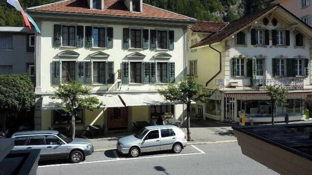 Ein mehrstöckiges Gebäude im traditionellen Baustil, mit einem zentralen Eingang und einem Balkon im zweiten Obergeschoss.