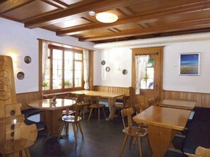 A dining area with wooden tables and chairs, large windows with curtains, and a wooden ceiling. - Rebstock (Meiringen)