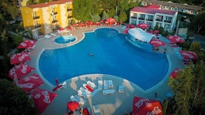 Un resort con una amplia piscina central rodeada de sillas de descanso y sombrillas, con vista al mar.