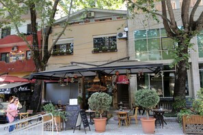 Una cafeteria a l'exterior amb taules i cadires, un cartell i plantes en testos.