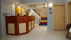 Un área de recepción con un escritorio de madera, una escalera de peldaños coloridos y una puerta cerrada.