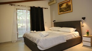 Un dormitorio con cama, mesita de noche, ventana con cortinas, aire acondicionado y un cuadro enmarcado en la pared.