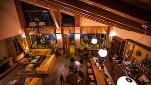 Ambiente spazioso con soffitto alto, travi in legno, un divano giallo, tavoli da pranzo e un'area bar con diversi oggetti.