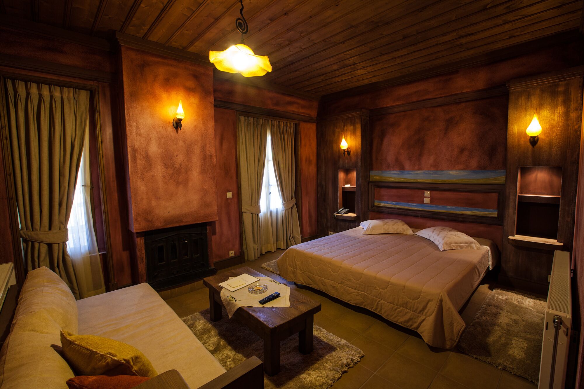 A cozy hotel room with two beds, a fireplace, and a painting on the wall.