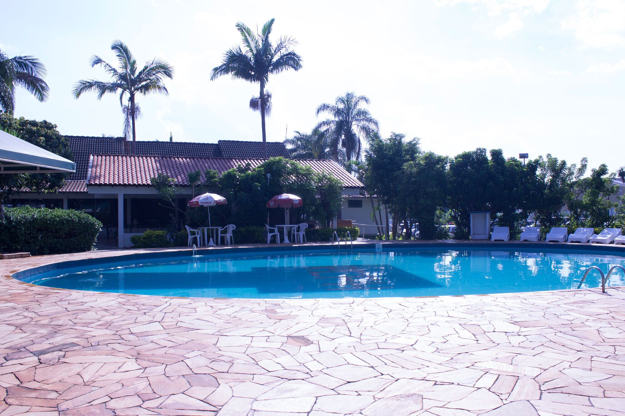 A swimming pool with a tiled deck, lounge chairs, and umbrellas.