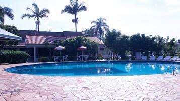 A swimming pool with a tiled deck, lounge chairs, and umbrellas.