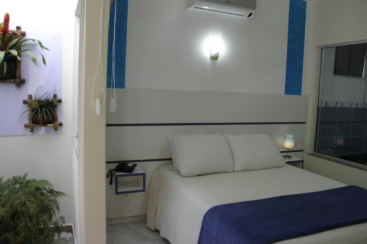 Ein Schlafzimmer mit Bett, Nachttisch, Lampe, Klimaanlage und Wandpflanzen.