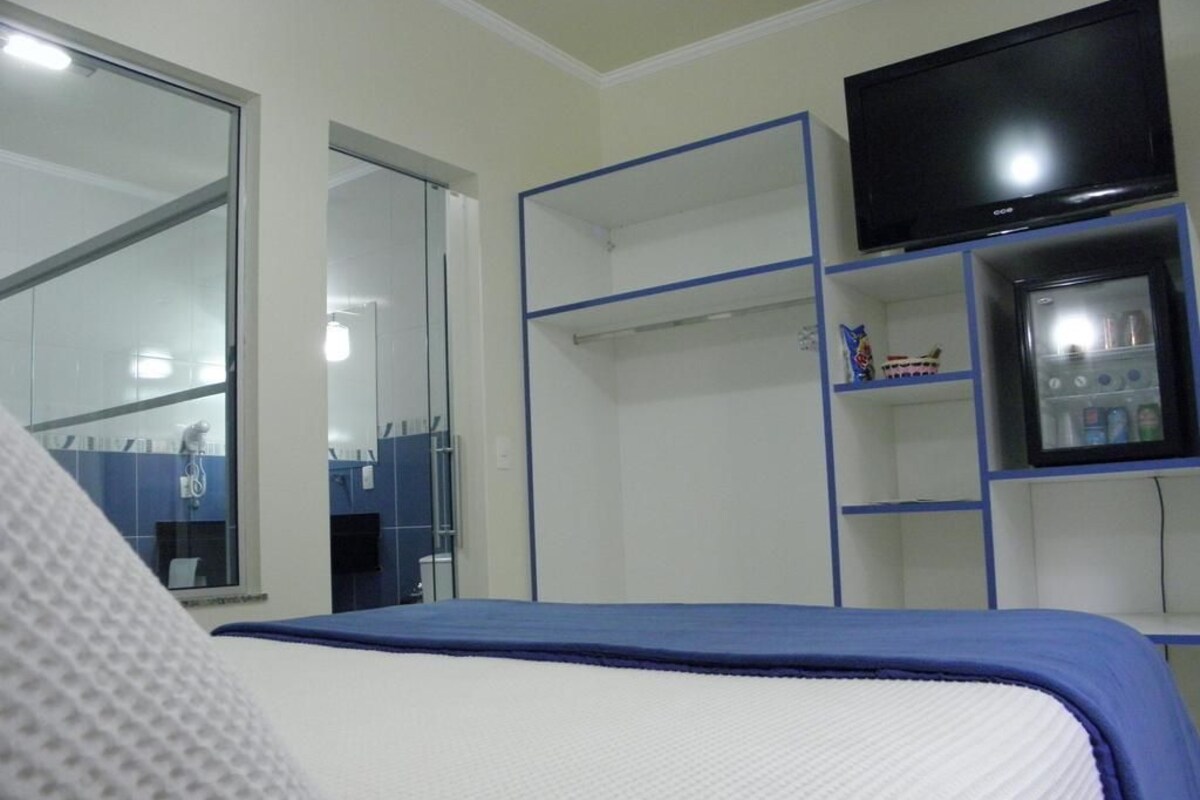 A bedroom with a bed, a television, a wardrobe, and a small fridge.