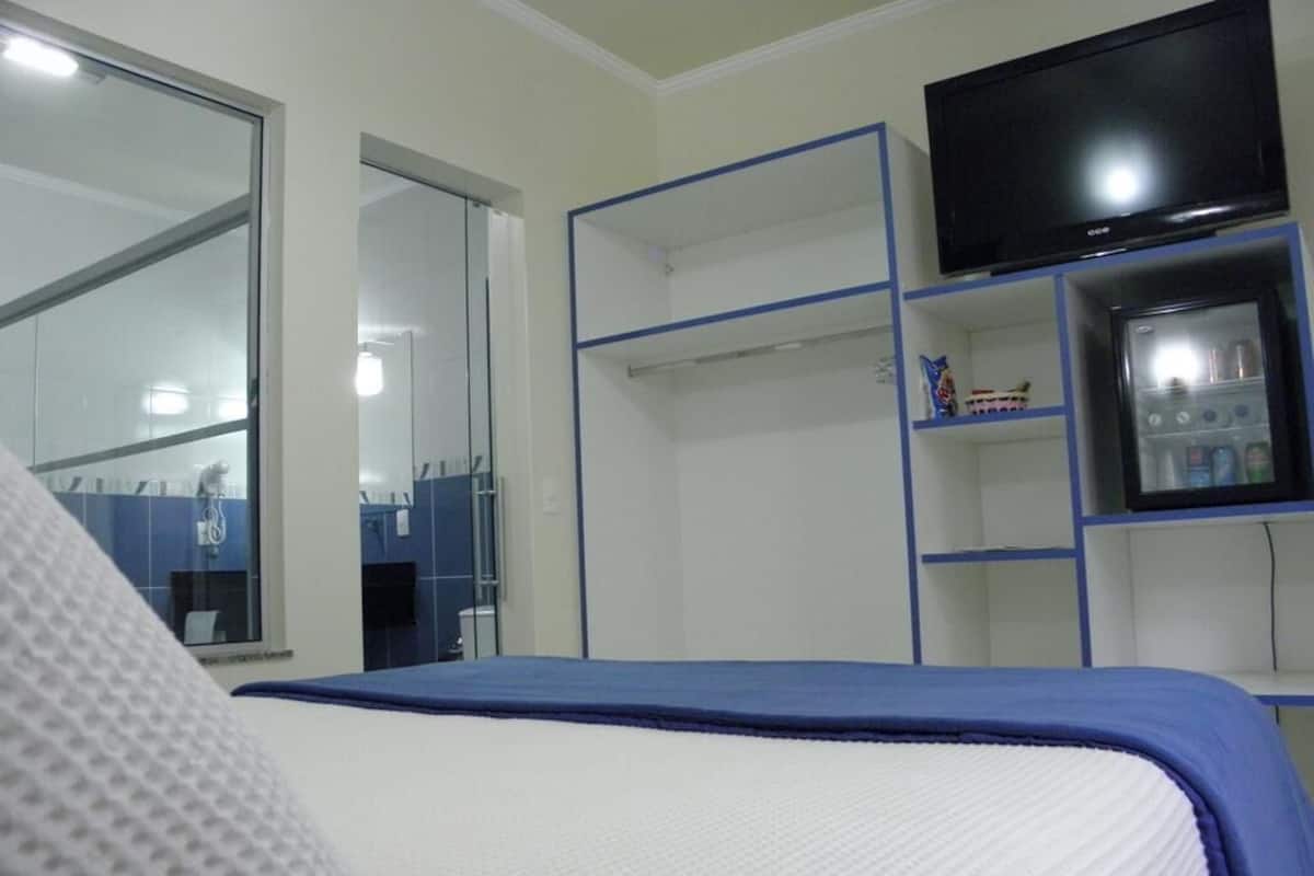 Ein Schlafzimmer mit Bett, Fernseher, Kleiderschrank und kleinem Kühlschrank.