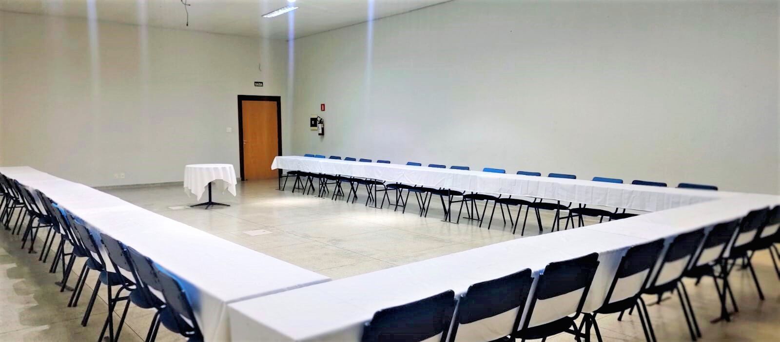 Un salón de conferencias con una larga mesa, filas de sillas y una puerta al fondo.