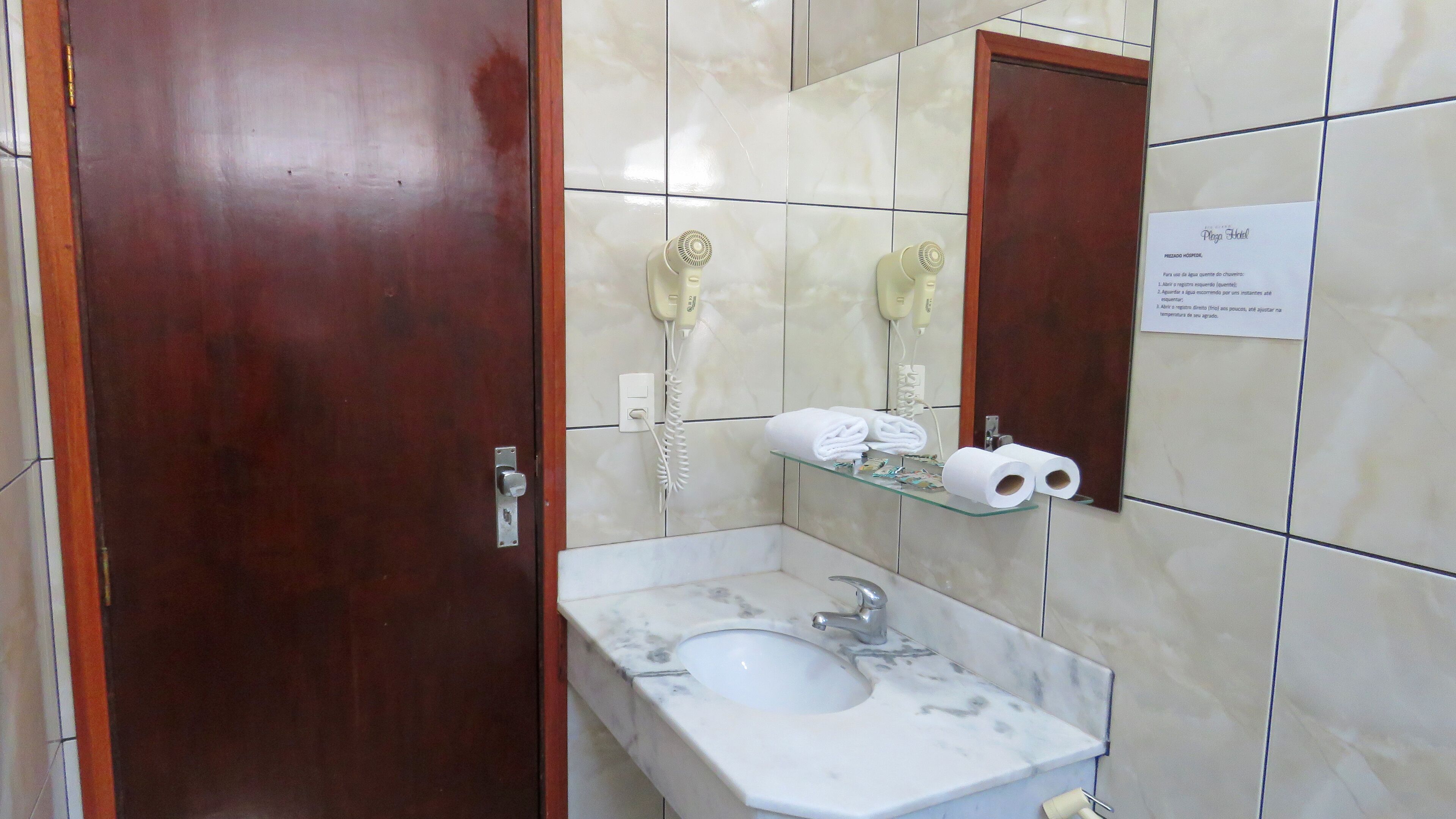 Une salle de bain avec un lavabo en marbre, deux sèche-cheveux, un porte-serviettes et un miroir.
