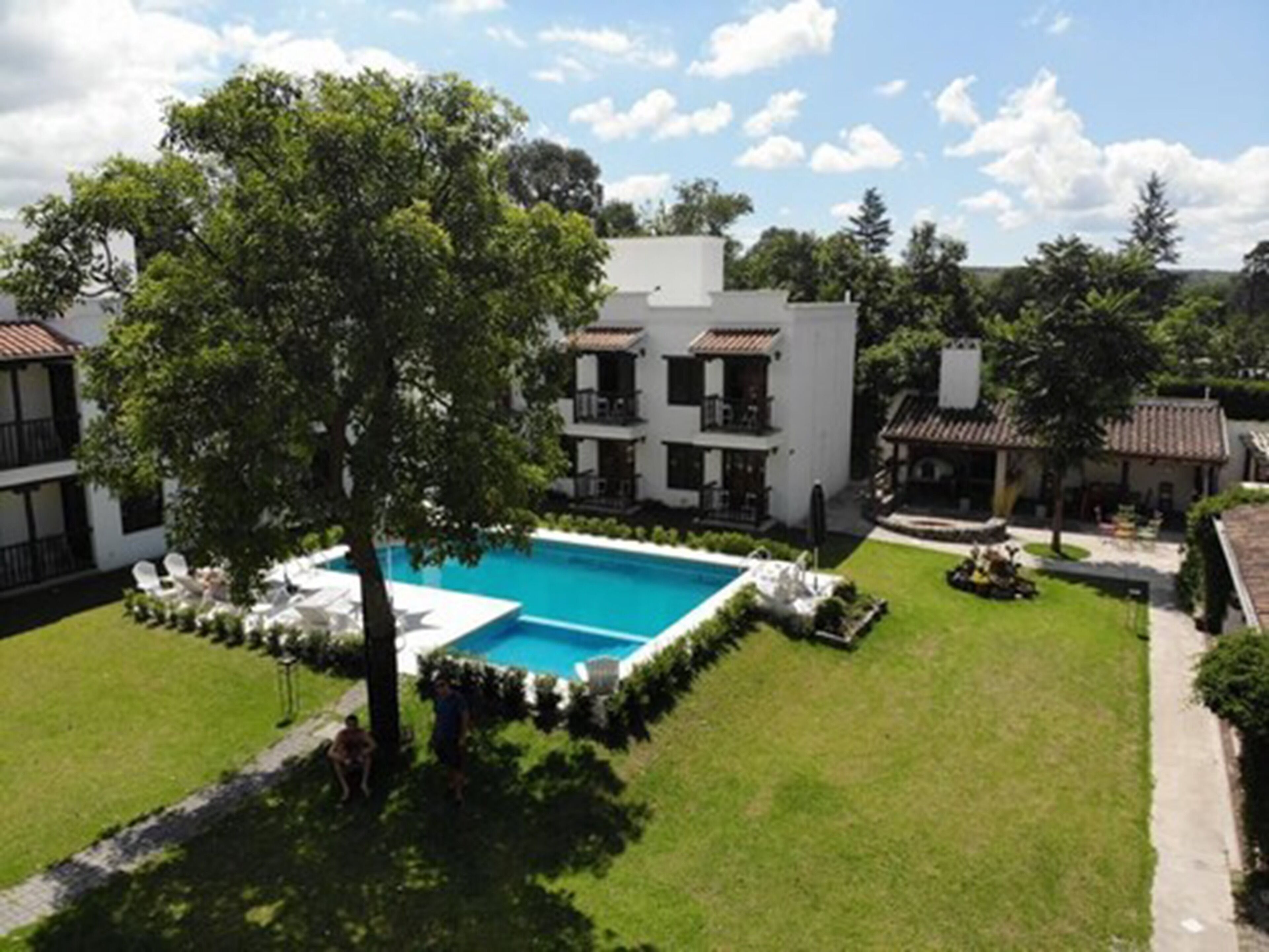 Una piscina circondata da un prato curato, con un edificio sullo sfondo dotato di balconi e tetto in tegole.