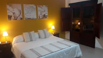 Quarto de hotel com cama, duas luminárias de cabeceira, mesa de apoio e guarda-roupa de madeira.