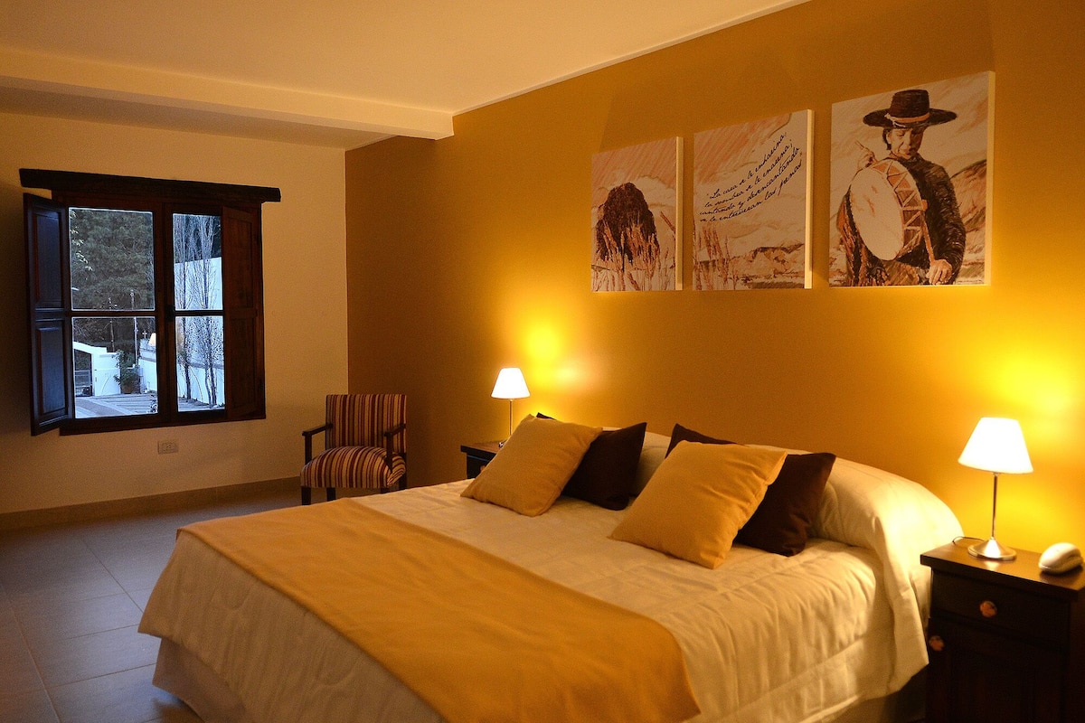 Ein Hotelzimmer mit einem großen Bett, zwei Nachttischlampen, einem Sessel und Bildern an der Wand.