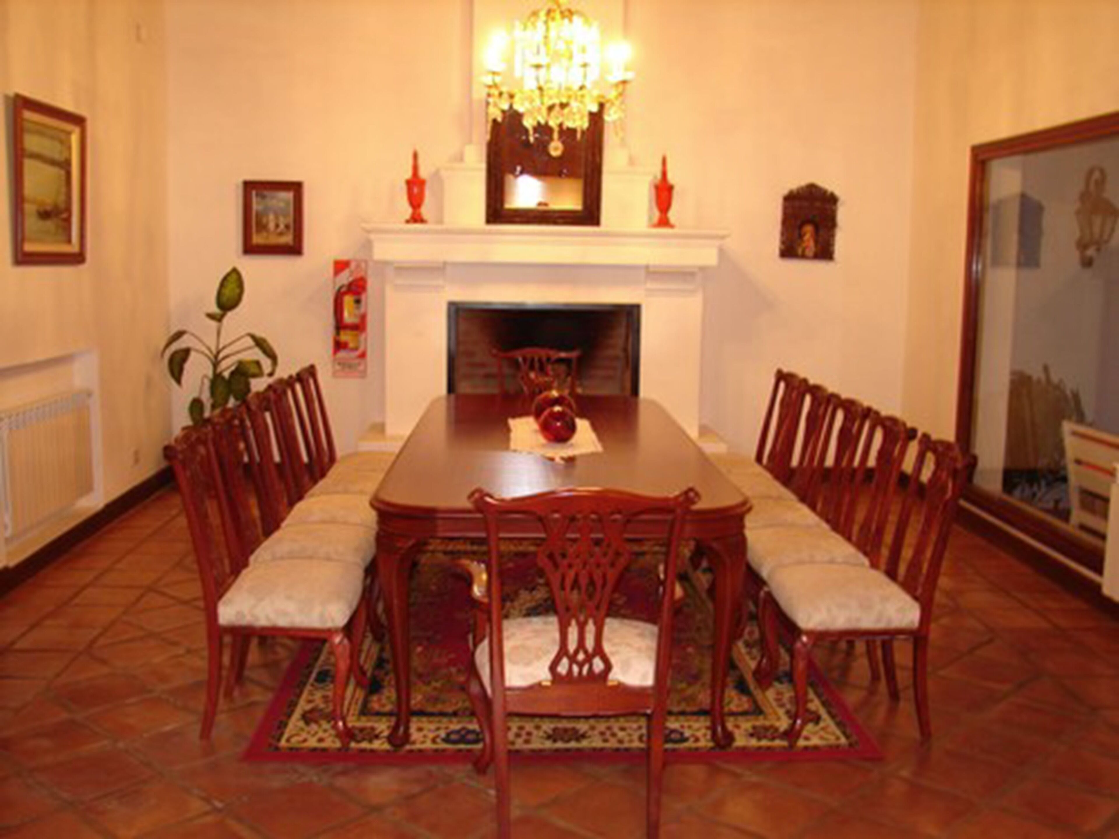 Une salle à manger avec une grande table en bois, six chaises, une cheminée et un lustre.