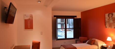 A hotel room with two beds, a desk, and a chair. There is a window with a view of the outside.