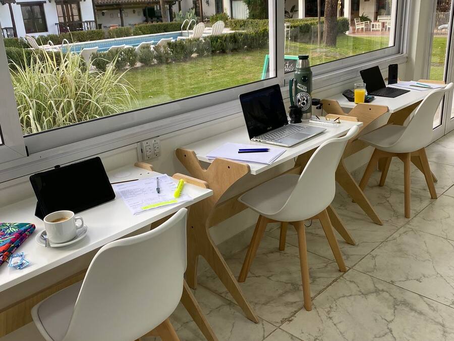 Une salle de classe avec des bureaux et des chaises disposés en rangées, de grandes fenêtres donnant sur une piscine et des bâtiments à l’extérieur.