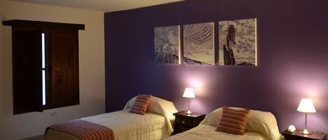 Una habitación de hotel con dos camas, un armario de madera y una pared morada con tres cuadros enmarcados.