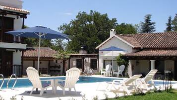 A pool area with lounge chairs and umbrellas, surrounded by buildings with tiled roofs.