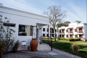 Un edificio moderno con fachada blanca, un jarrón marrón grande y un caballete pequeño con un lienzo en blanco.