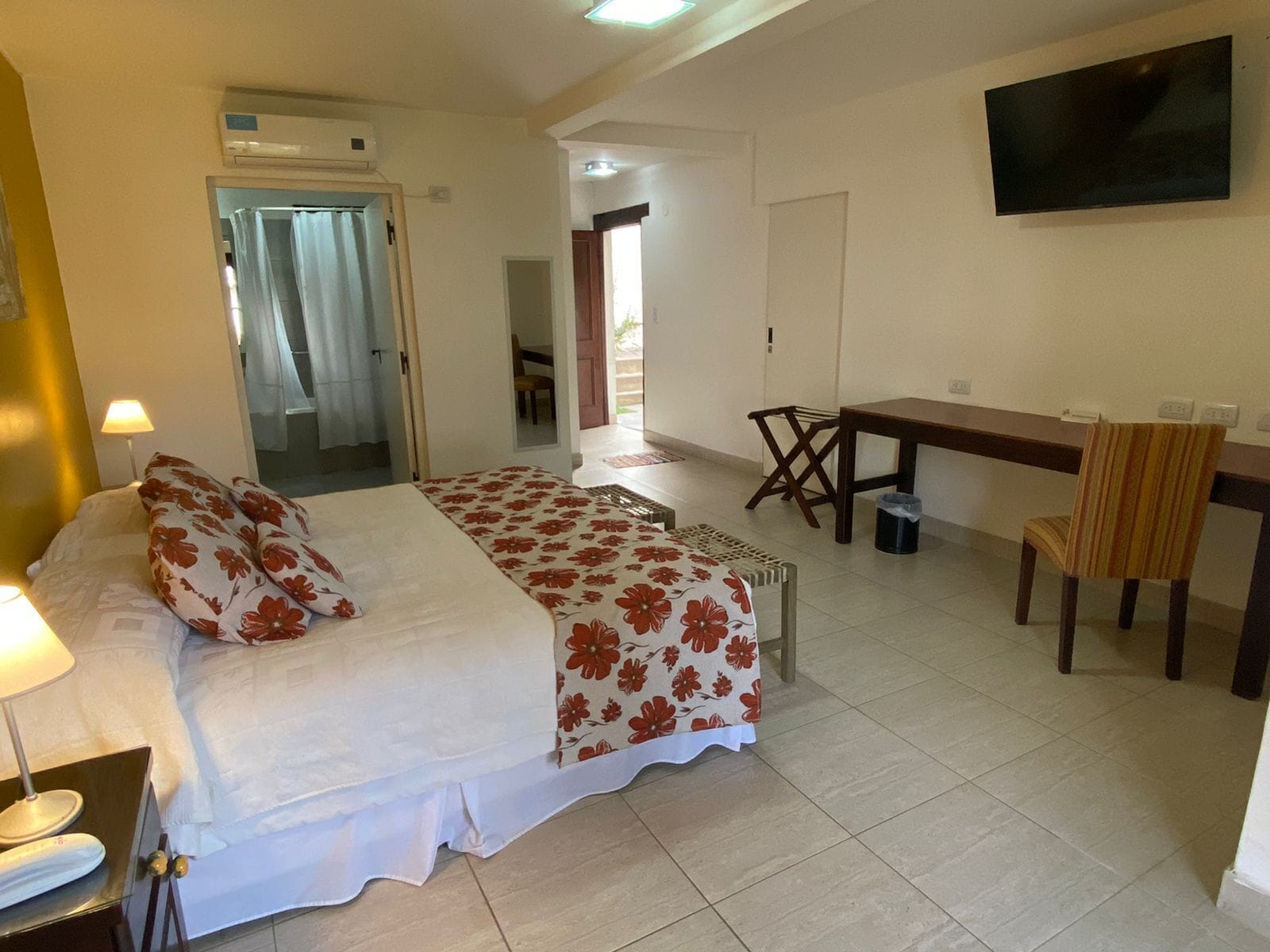 A hotel room with a bed, a desk, a chair, a TV, and a bathroom visible through an open door.