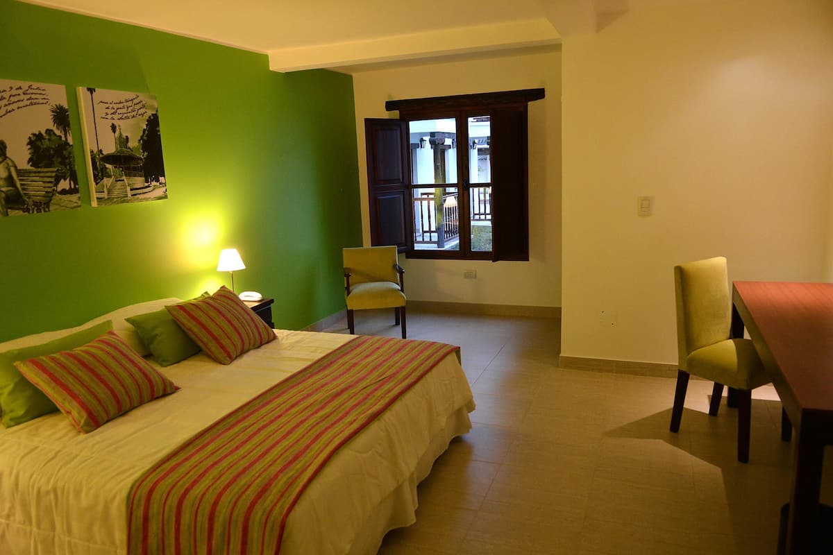 Ein Zimmer mit Bett, Stuhl, Tisch, Fenster und Lampe.