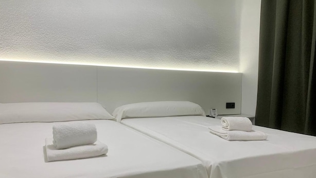 Quarto de hotel com duas camas, cada uma com toalhas brancas dobradas.