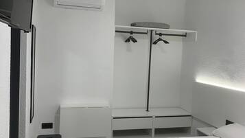 Une chambre d’hôtel minimaliste comprenant un lit, un petit tabouret, une armoire avec un miroir et un téléviseur à écran plat fixé au mur.