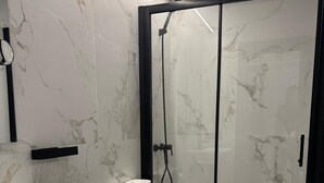 Um banheiro moderno com painel de fundo de mármore branco, pia branca, vaso sanitário e área de chuveiro com box de vidro.