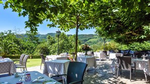 An outdoor dining area with tables and chairs, set against a backdrop of lush greenery and hills. - Jardins de Bakea (Biriatou)