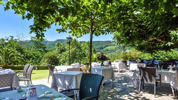 An outdoor dining area with tables and chairs, set against a backdrop of lush greenery and hills. - Jardins de Bakea (Biriatou)