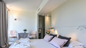 A hotel room with a neatly made bed, two chairs, a small table with a vase of flowers, and a door leading to a bathroom. - Jardins de Bakea (Biriatou)