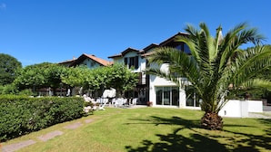 A two-story building with a garden in front, featuring a palm tree and a well-maintained lawn. - Jardins de Bakea (Biriatou)