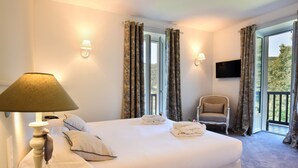 A hotel room with a large bed, a chair, a TV, and a balcony with curtains. - Jardins de Bakea (Biriatou)